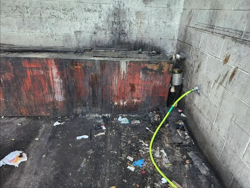 Same dumpster pad dirty with litter and stained walls