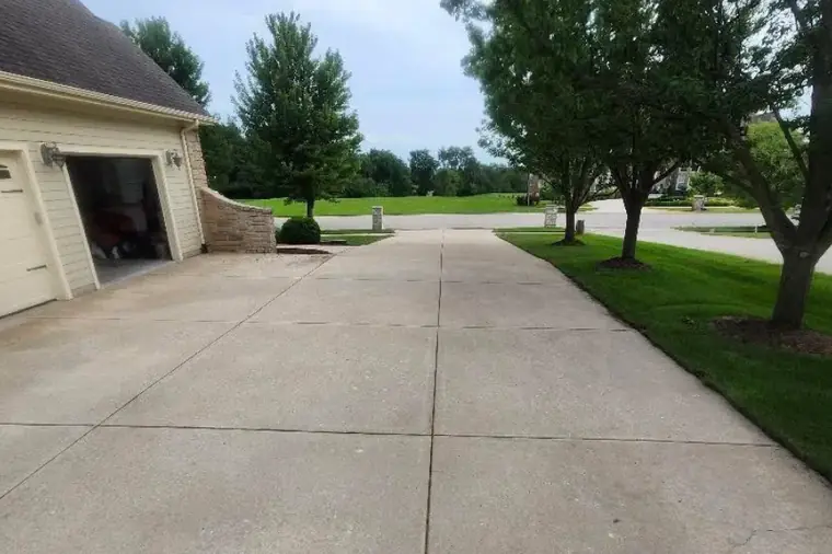 Wide clean concrete driveway beside a house and green lawn